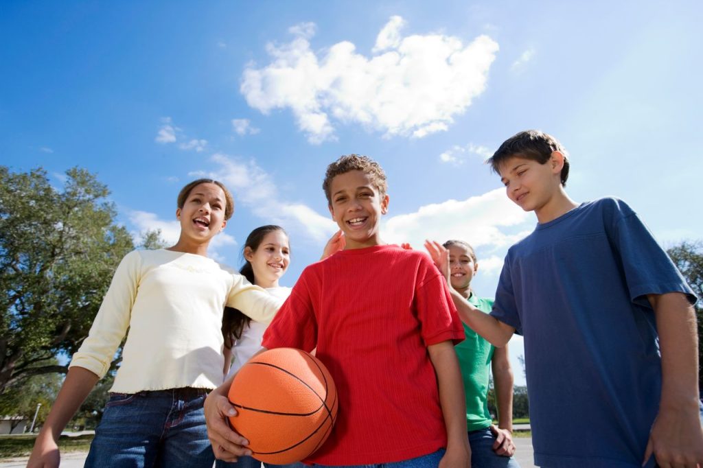 A joyful group of diverse kids playing with a basketball under a bright blue sky.