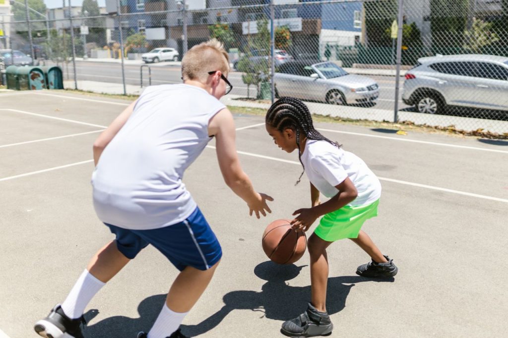 Two children playing an energetic game of basketball on an outdoor court during the day.