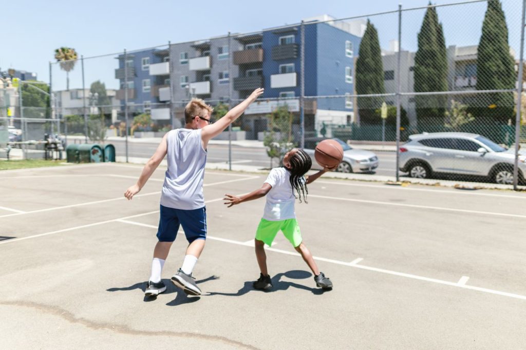 Two children enjoy a lively game of basketball outdoors on a sunny day.
