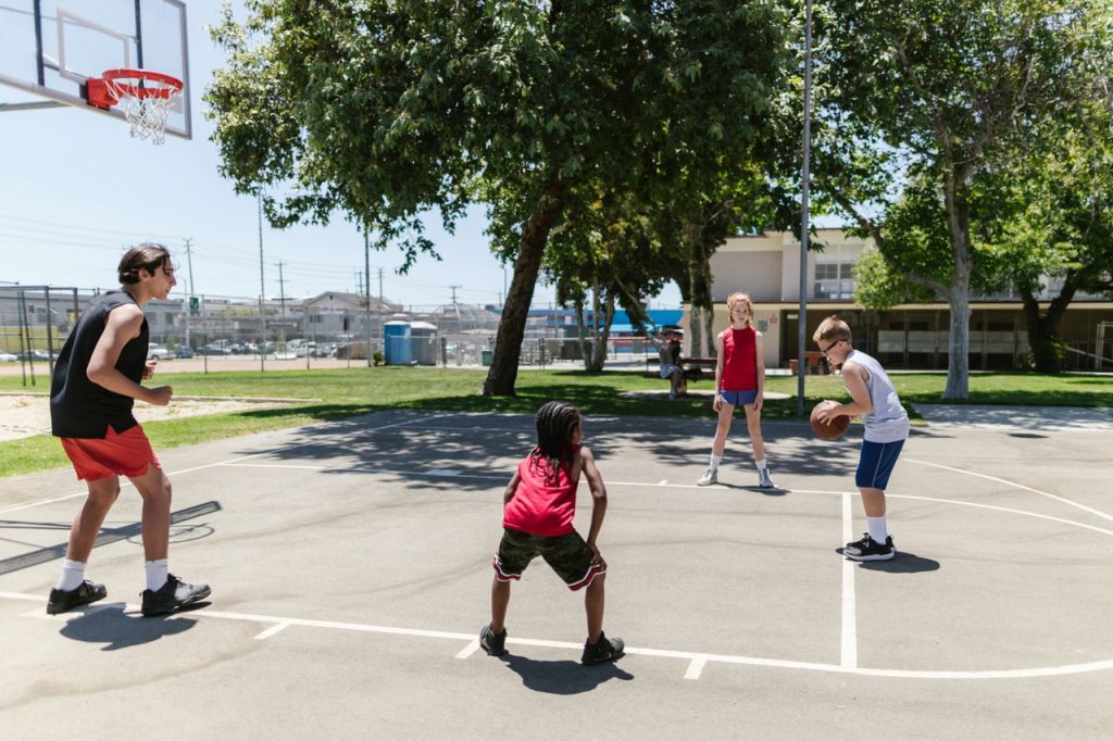 Group of kids playing basketball on an outdoor court, enjoying a sunny day.